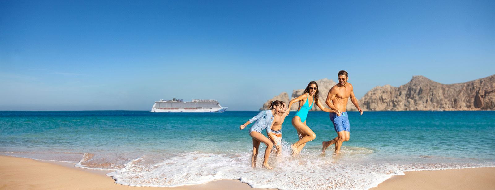 Family frolicking on shore and Norwegian Cruise Line ship in background